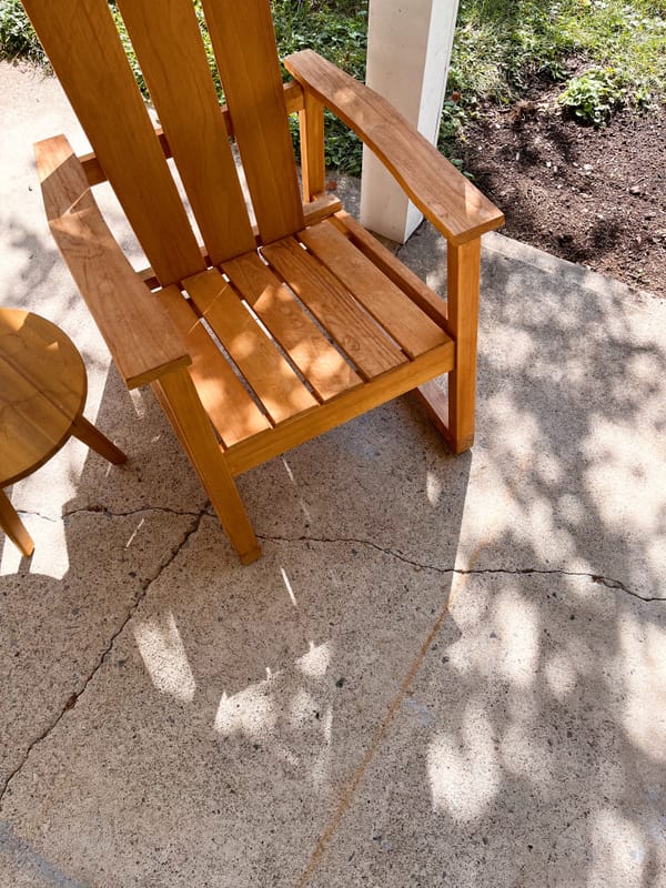 Adirondack chair in dappled shade on cracked concrete